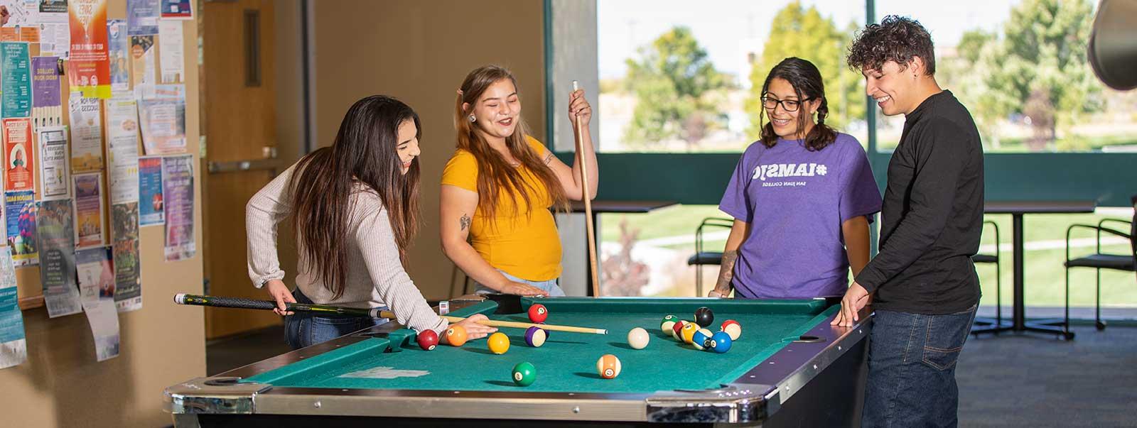 Four students playing billiards and laughing